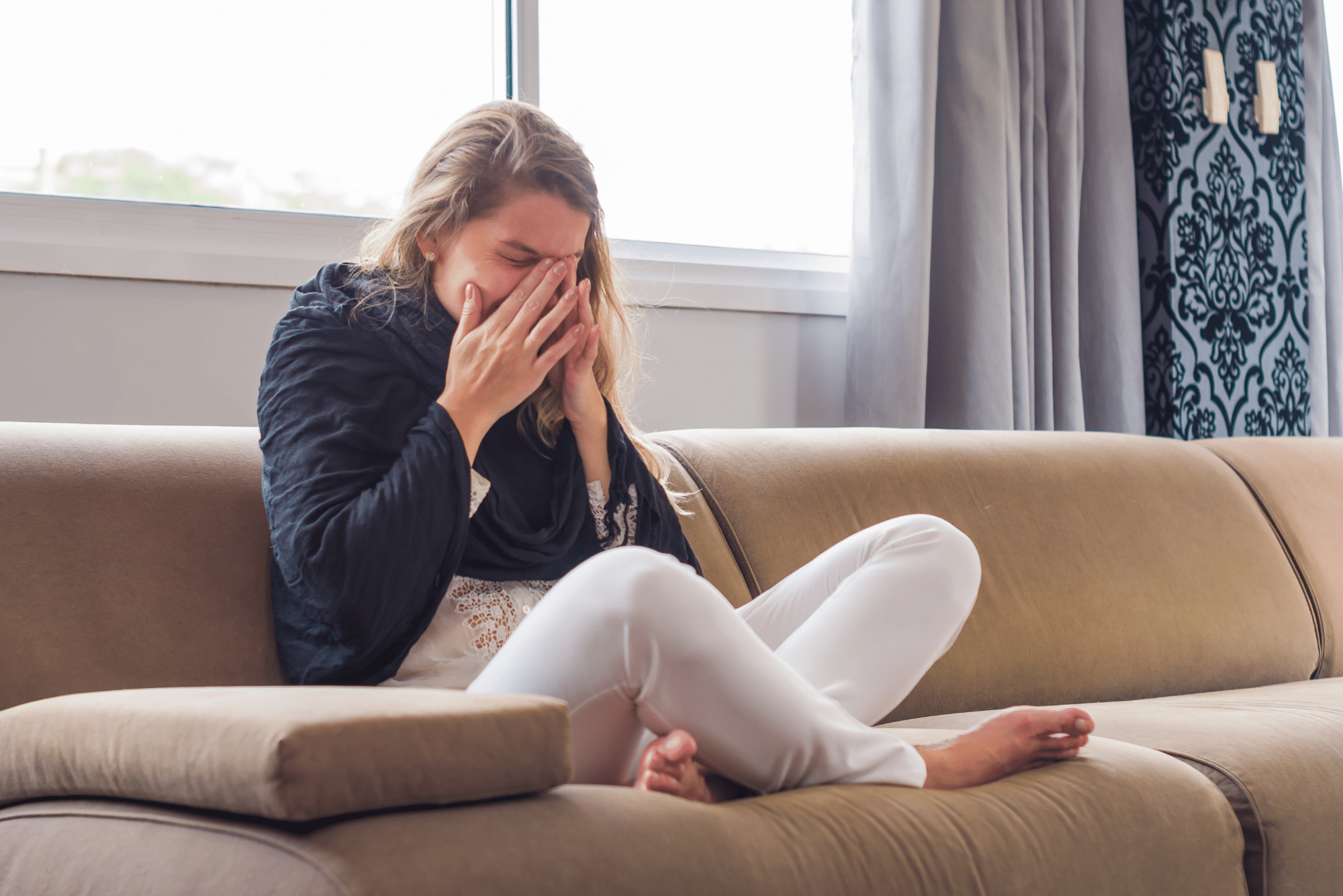 woman with allergies sitting on a couch massaging a headache