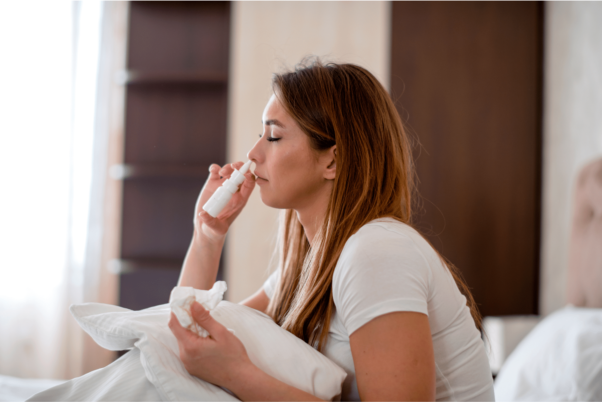 A woman with tissue in hand closes her eyes and uses a nasal spray for relief from her nasal polyps.