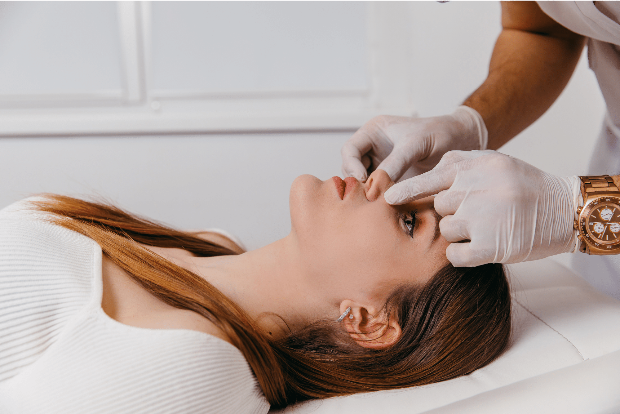 A brunette woman with a deviated septum reclines while a doctor examines her nose from above.