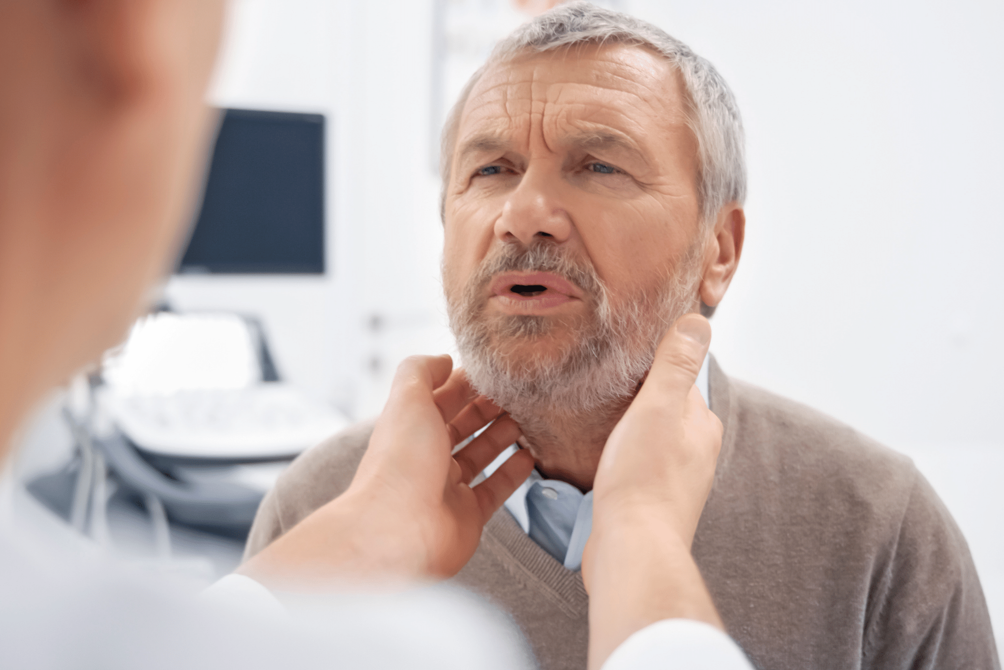 A doctor palpates for salivary gland tumors under the jaw of a bearded older gentleman.