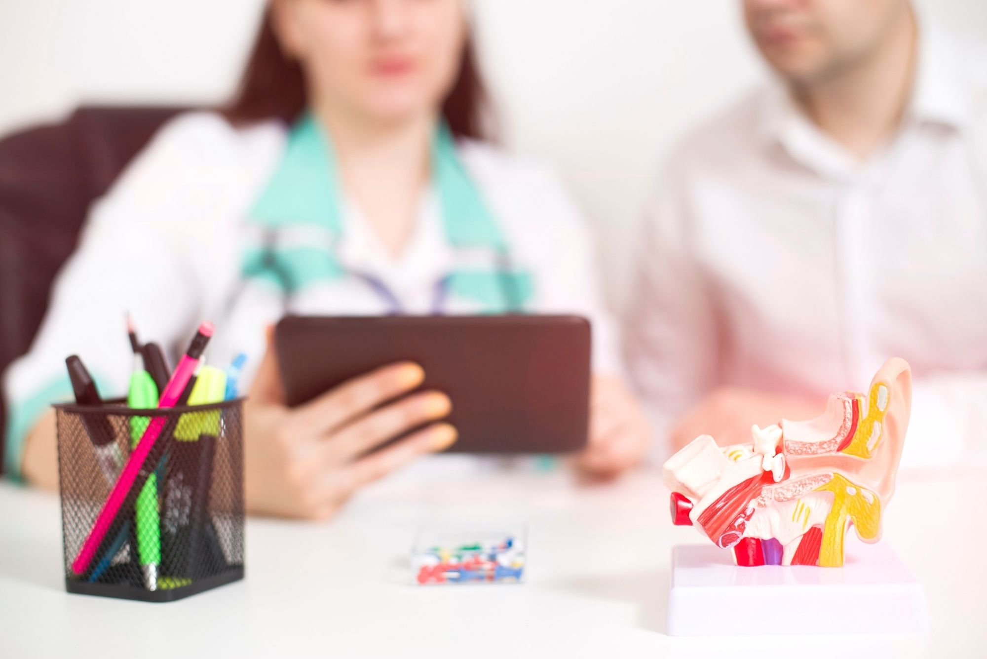 A female doctor talks with a male patient at a desk with medical models and a pen container.