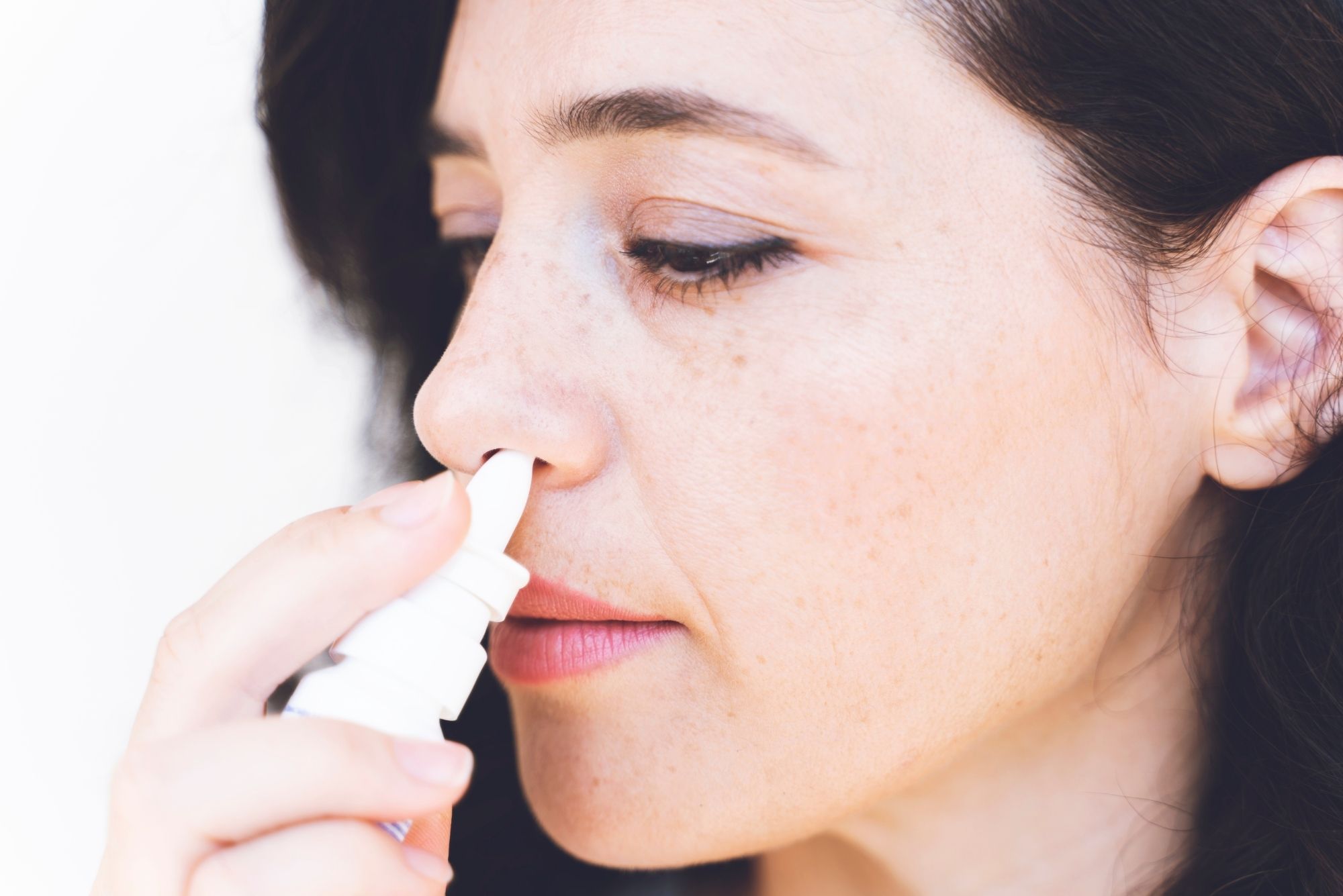 A woman with brown hair uses a decongestant nasal spray for her eustachian tube dysfunction.