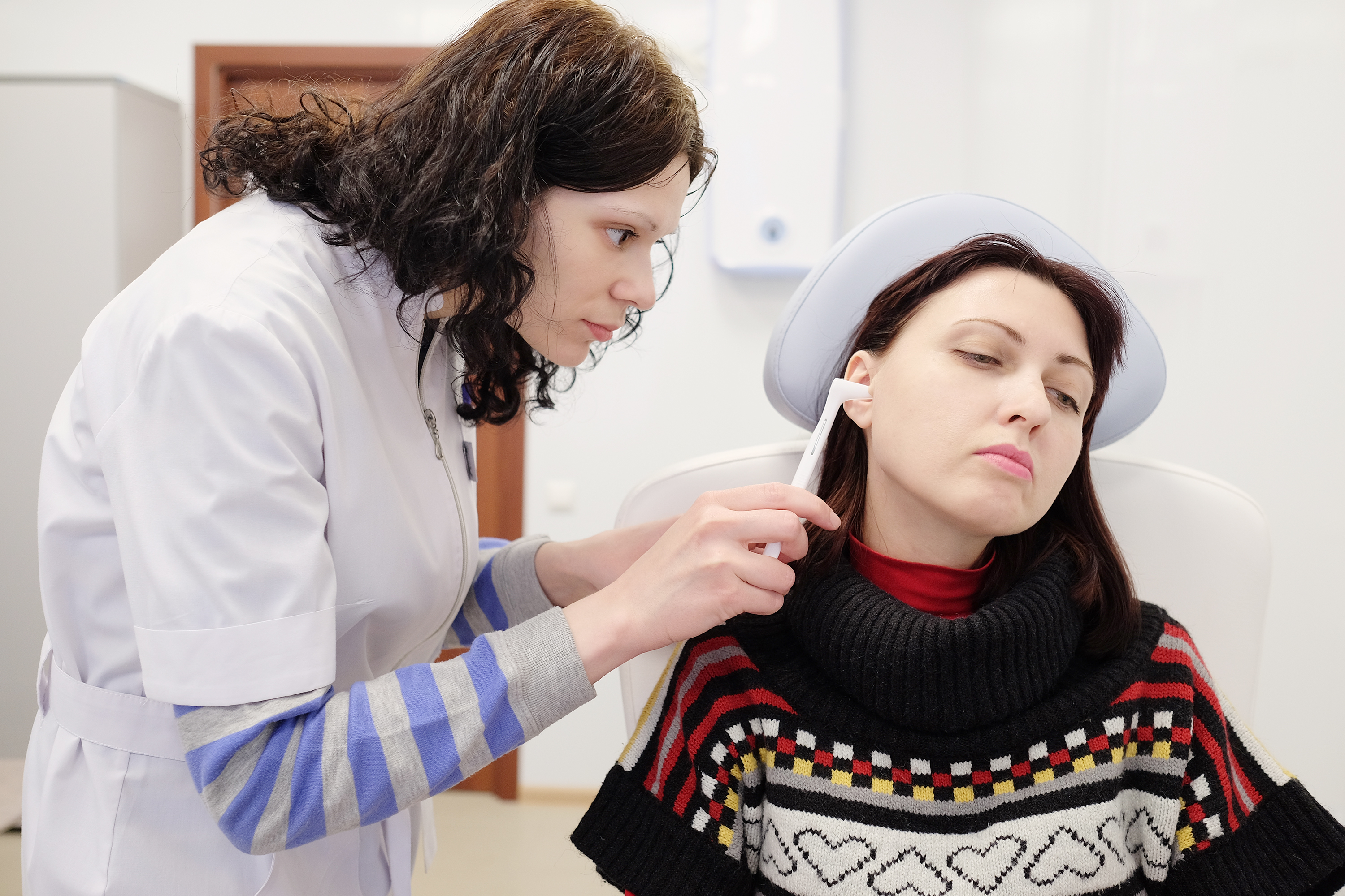 A female doctor examines the ear of a female patient suffering from chronic eustachian tube dysfunction.
