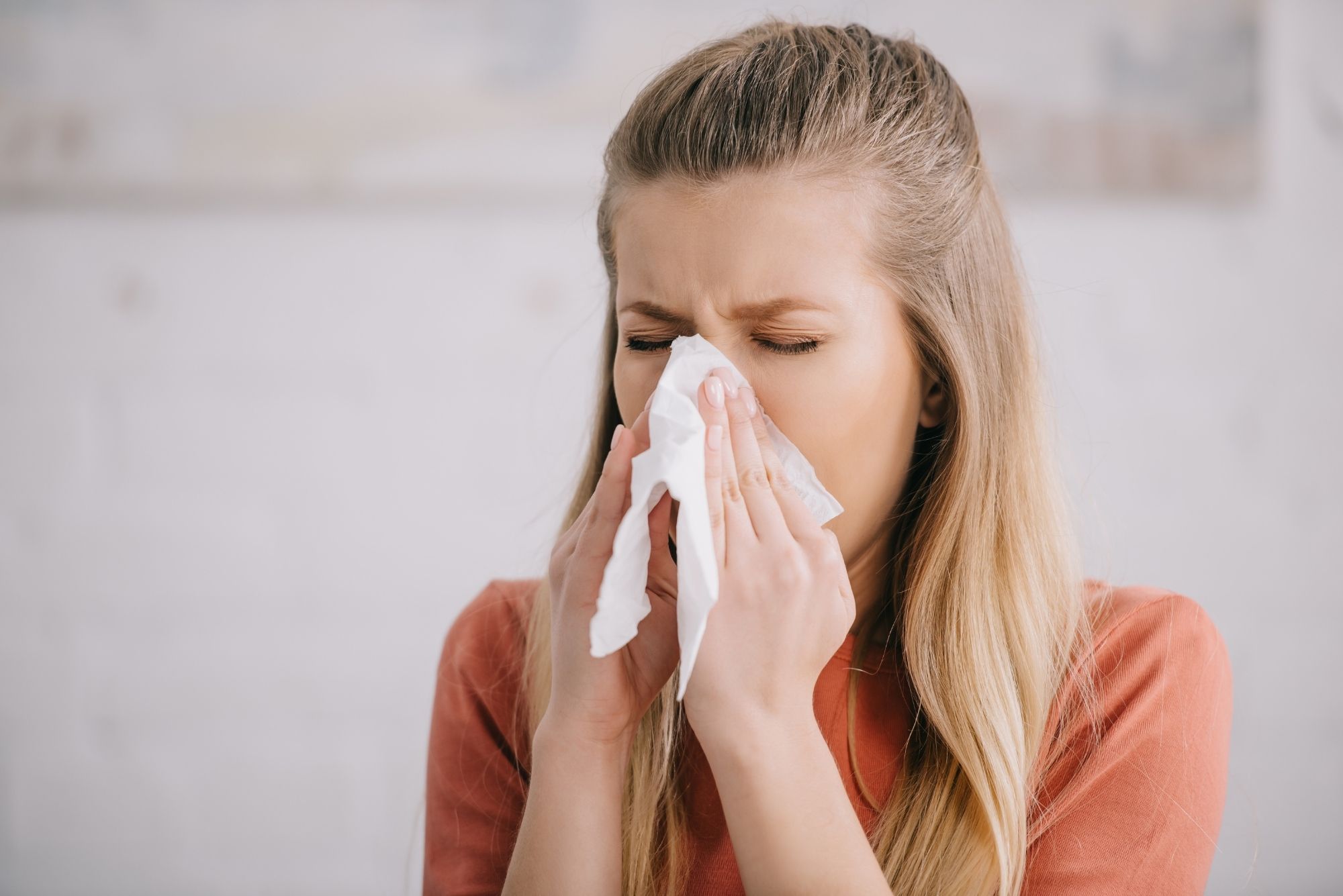 A blonde woman considering balloon sinus dilation holds a tissue to her nose and scrunches her eyes shut.