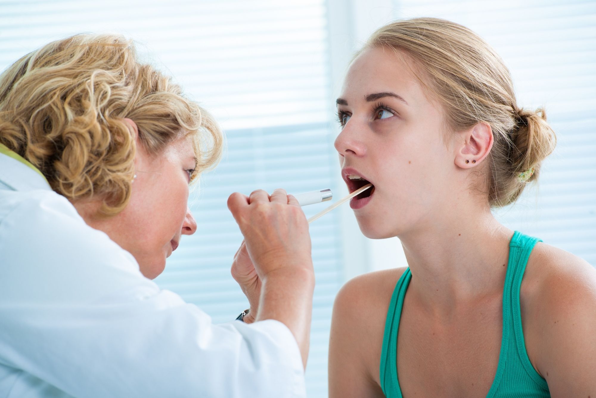 An ENT doctor examines a patient's throat for tonsillectomy complications.