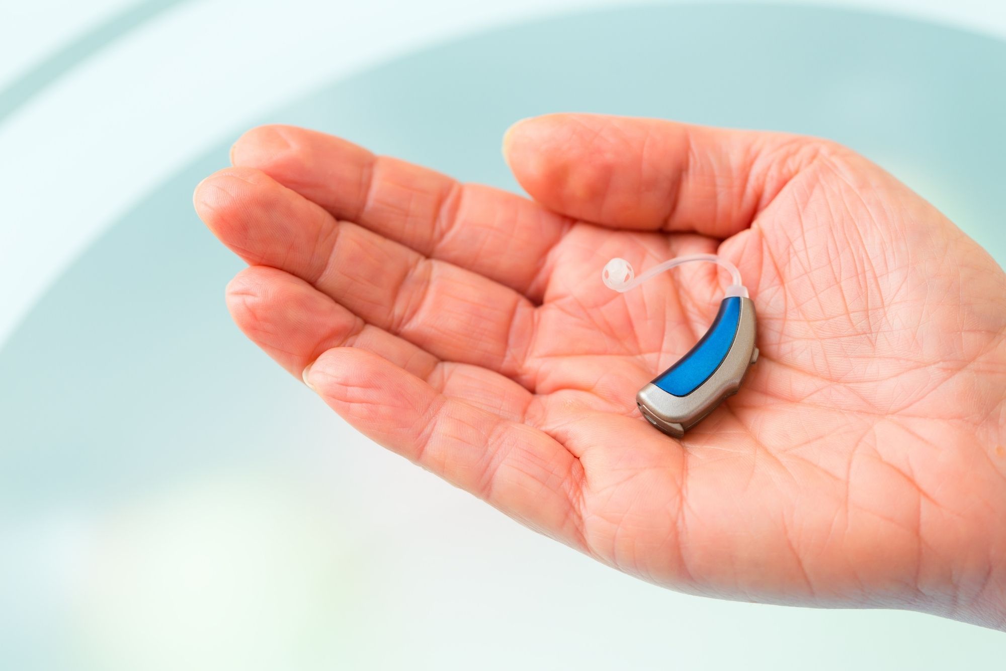 A hand holds a small blue hearing aid in its palm, representing ideas on how to prevent hearing loss.