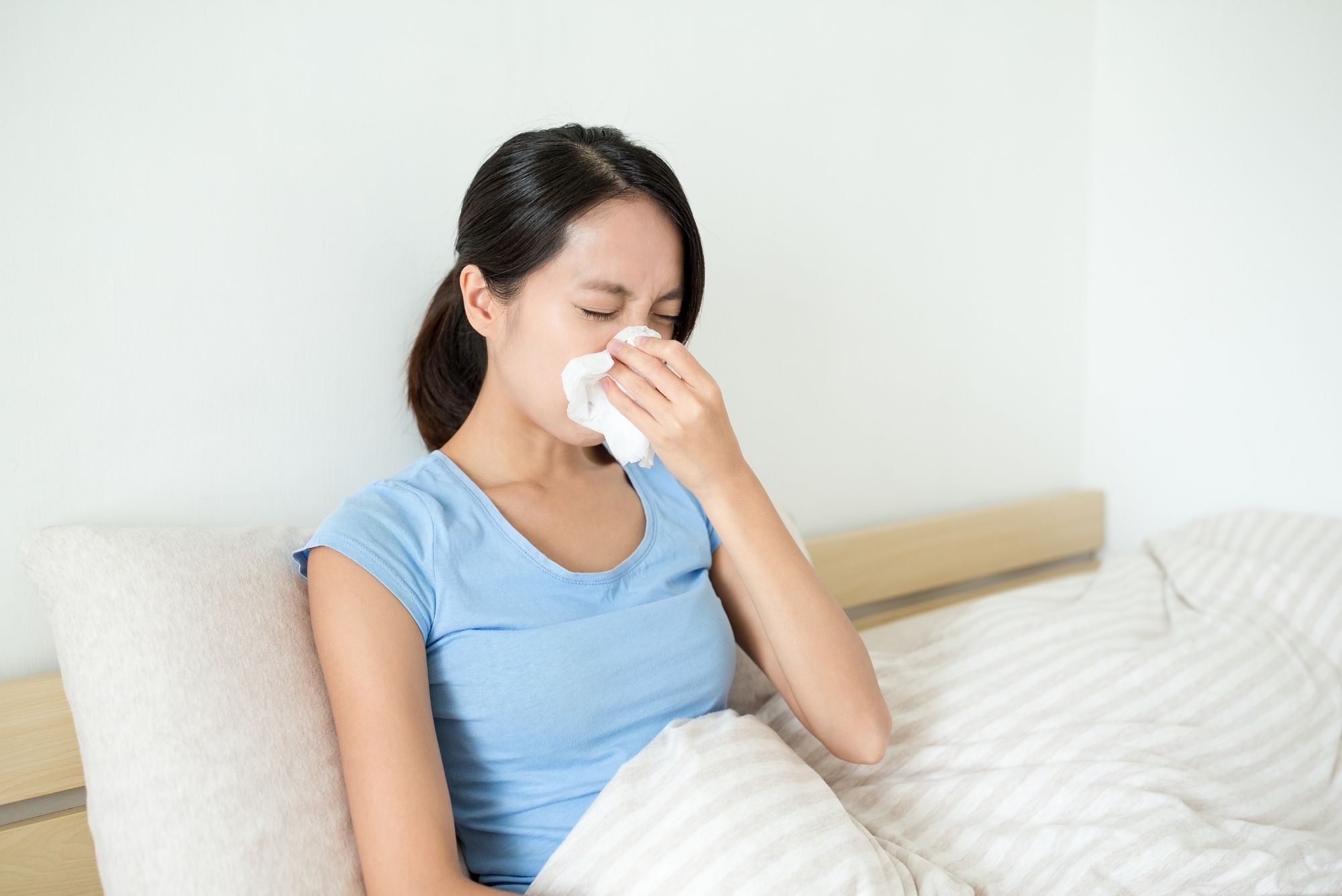 A woman blowing her runny nose considers the pros and cons of RhinAer vs ClariFix.