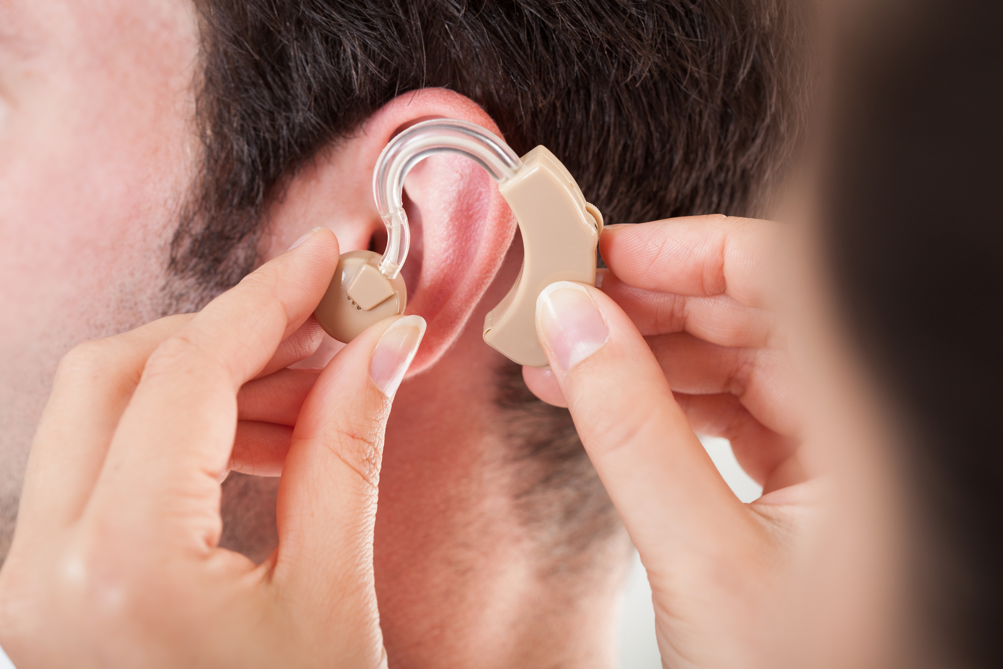 An ENT doctor explains to the patient what level of hearing loss requires a hearing aid while putting the hearing aid on.