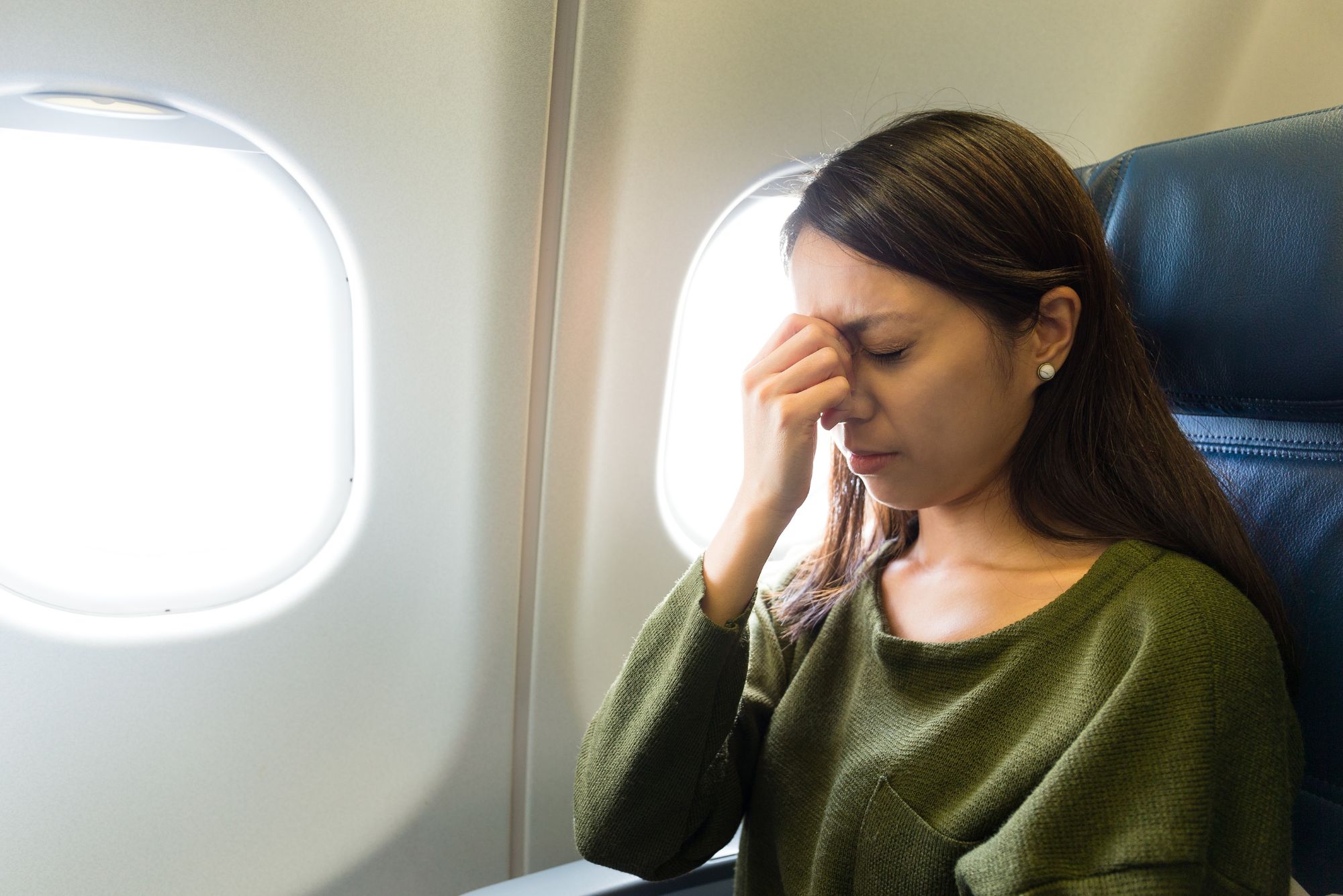 A woman flying with a sinus infection sits on the plane pinching the bridge of her nose.