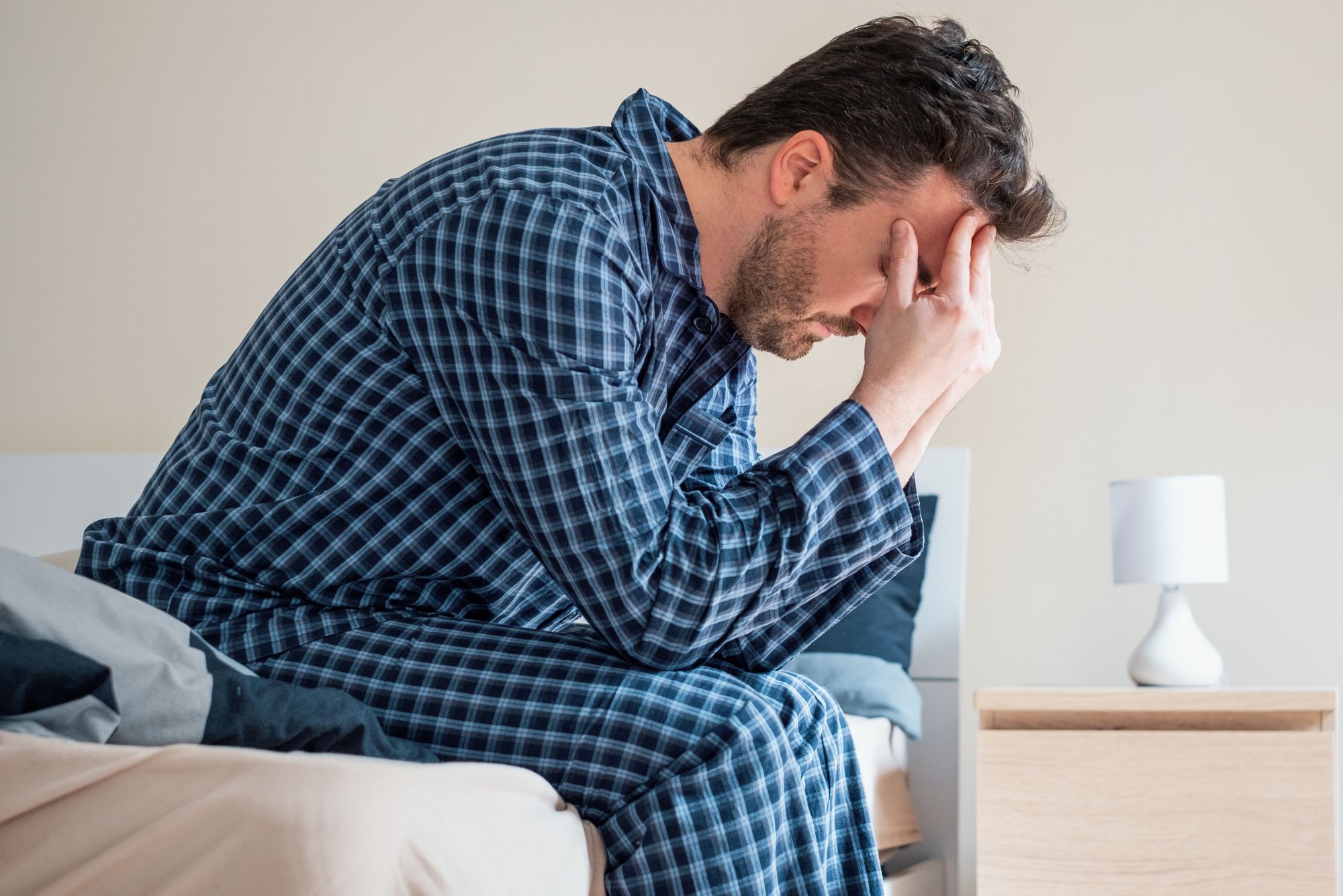 A man sits up on his bed, struggling to sleep because he can't breathe through his nose when lying down.