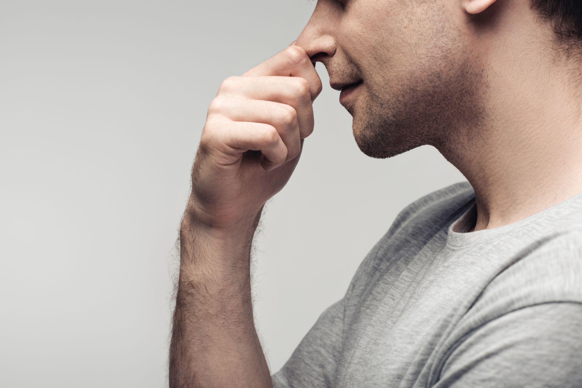 A man wearing a grey shirt holds his nose, which is stuffy due to swollen turbinates.