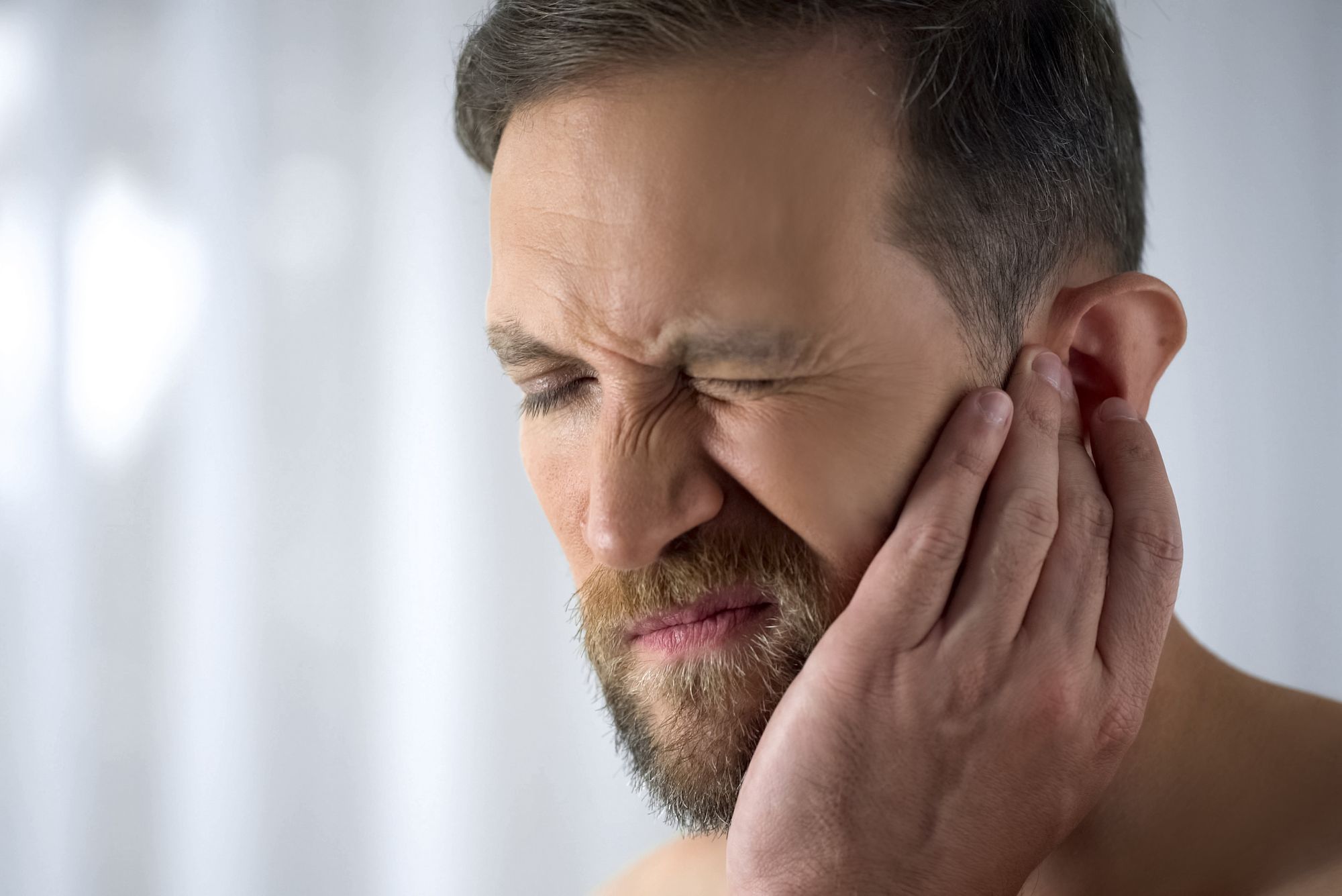 A man holds his ear while experiencing sudden hearing loss in one ear.