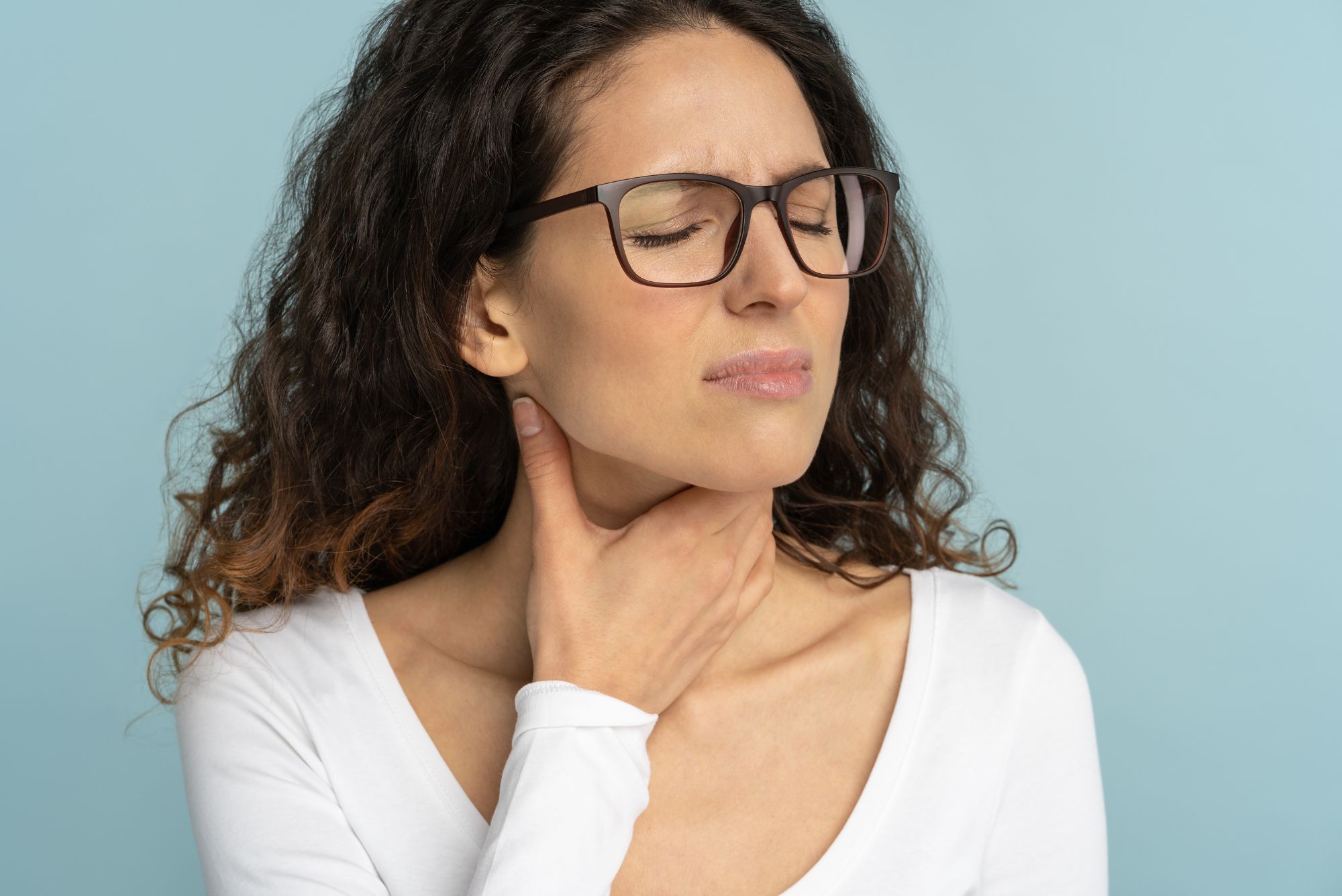 A woman holds her swollen tonsils, wincing in pain.