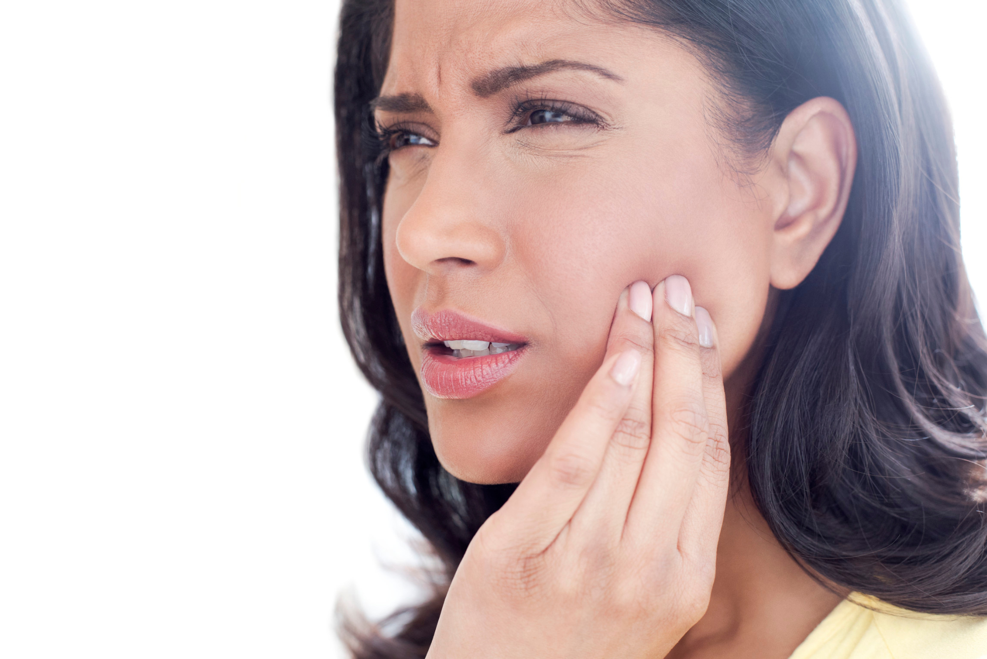 A dark-haired woman winces in pain while holding her jaw, thinking about getting botox for TMJ.