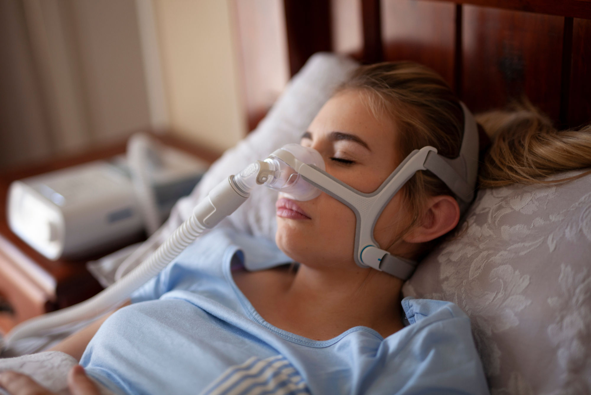 A woman lays in bed wearing her CPAP machine, thinking about all the different treatments for mild obstructive sleep apnea.
