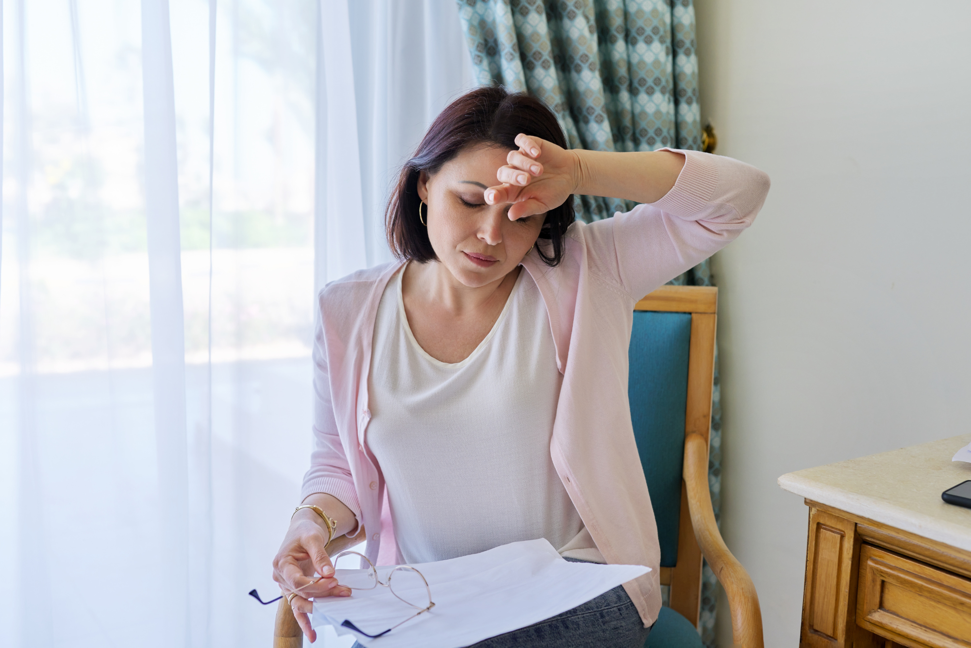 A seated woman holds her forehead head while experiencing a headache after Botox.