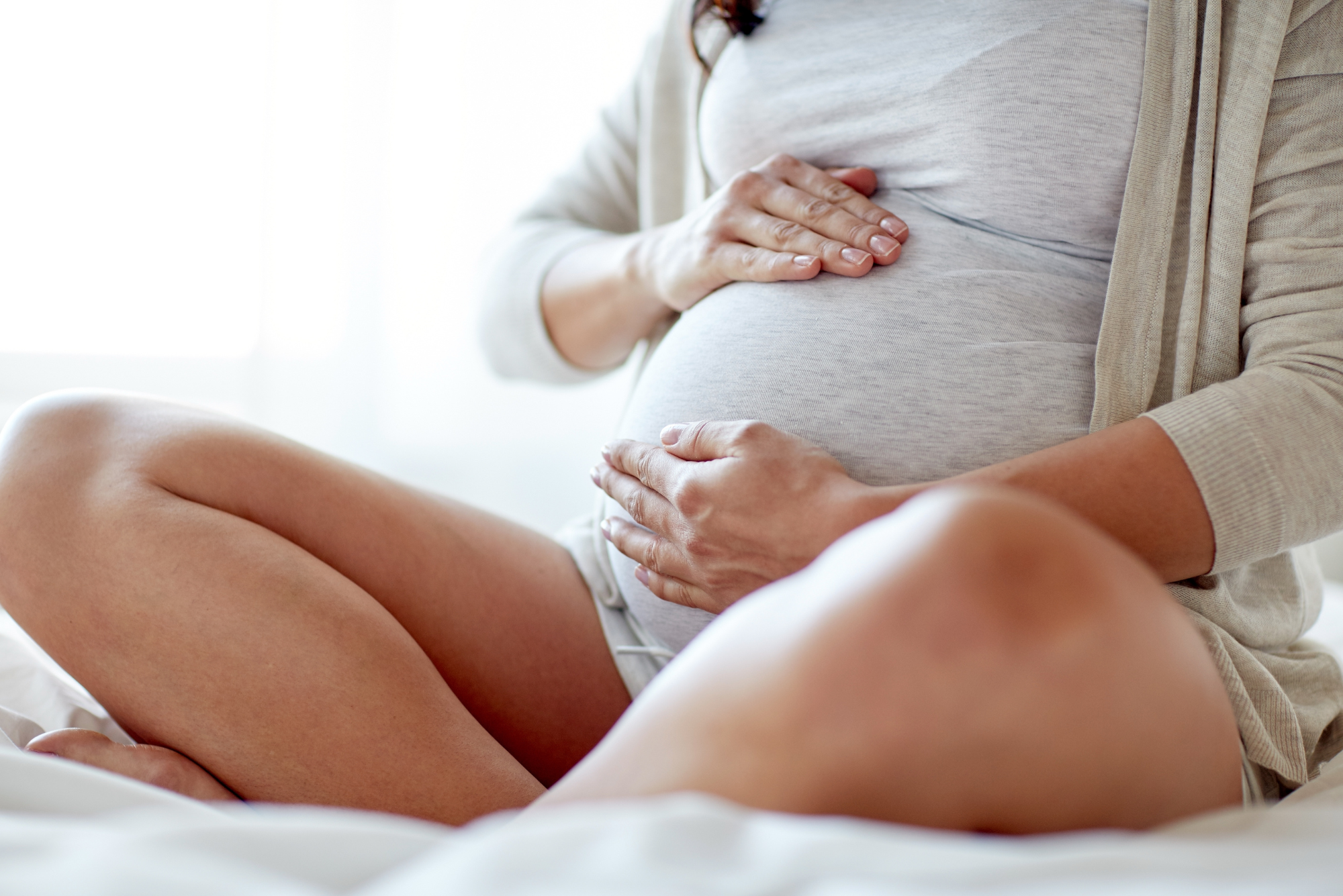 A pregnant woman holds her stomach while sitting before going to her ENT doctor to ask if she can get botox while pregnant.