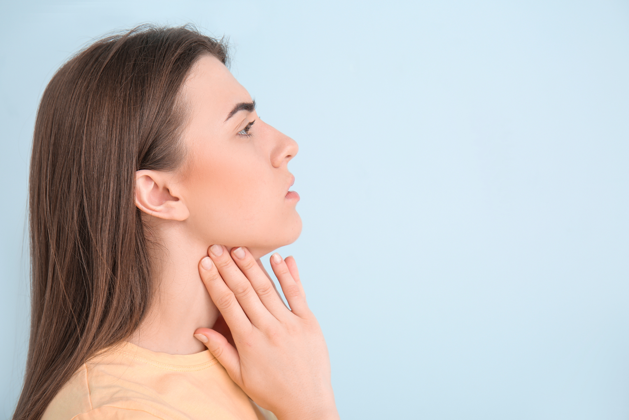 A profile shot of a woman palpating her throat before getting an excision biopsy of her lymph nodes.