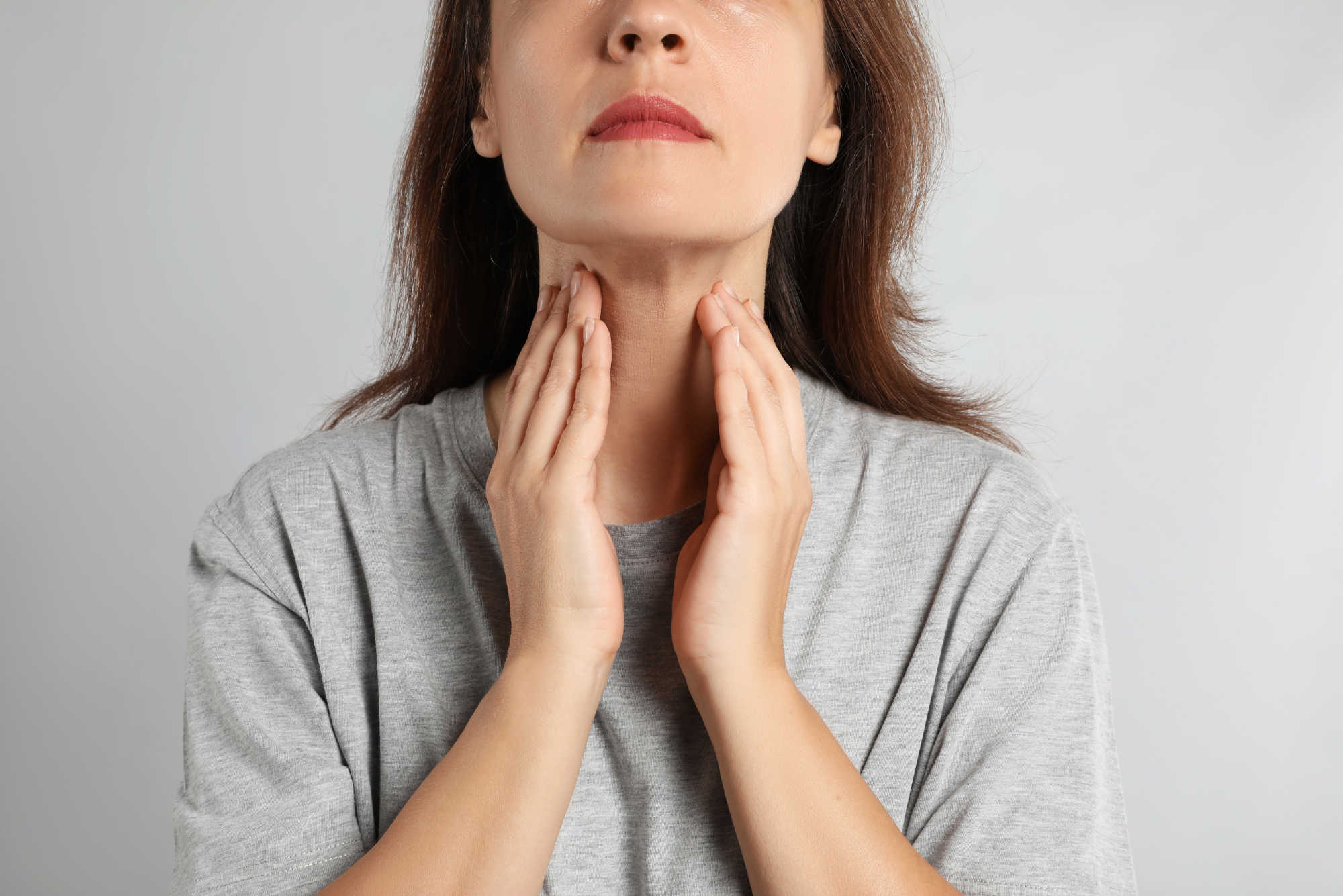 A woman who needs a parathyroid exploration procedure holds her throat between her hands.