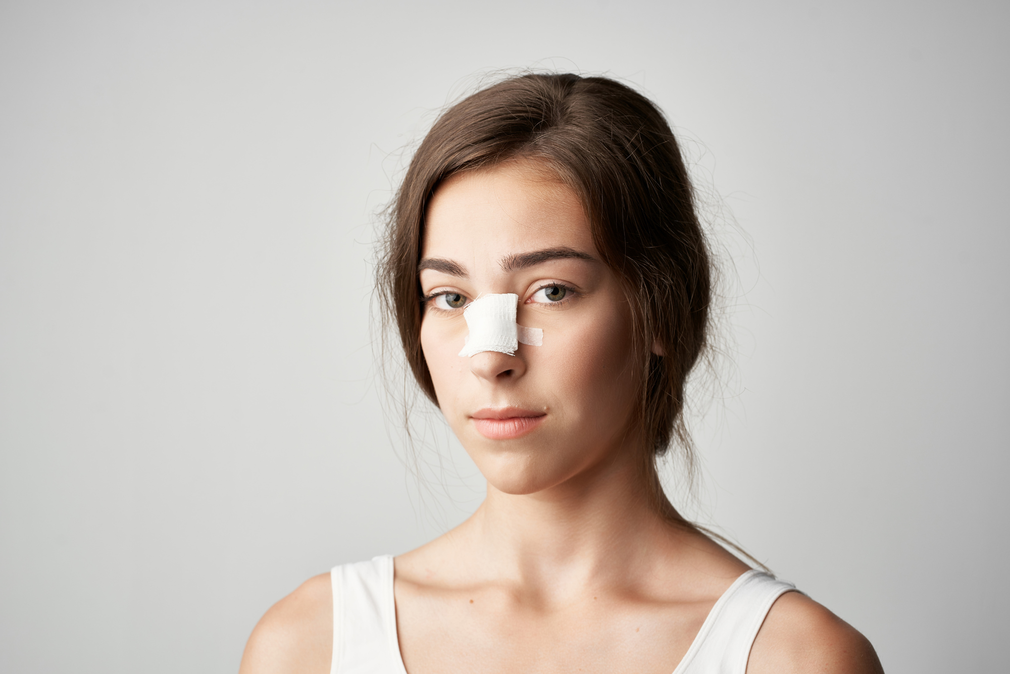 A teenager has a bandage taped over top of her nasal fracture because she just had a closed reduction procedure done.
